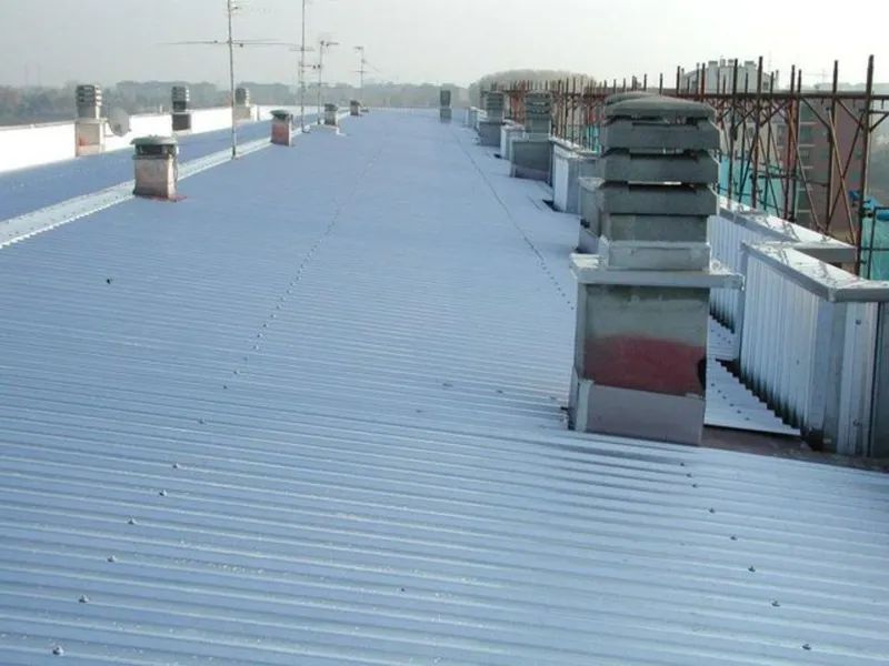 Tetto innevato con pannelli metallici blu e diverse ciminiere sotto un cielo grigio