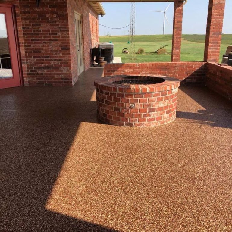 A brick patio with a matching circular fire pit, featuring a textured brown aggregate floor under a covered porch.