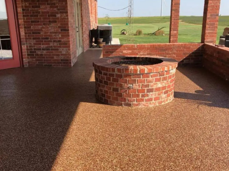 A brick patio with a matching circular fire pit, featuring a textured brown aggregate floor under a covered porch.