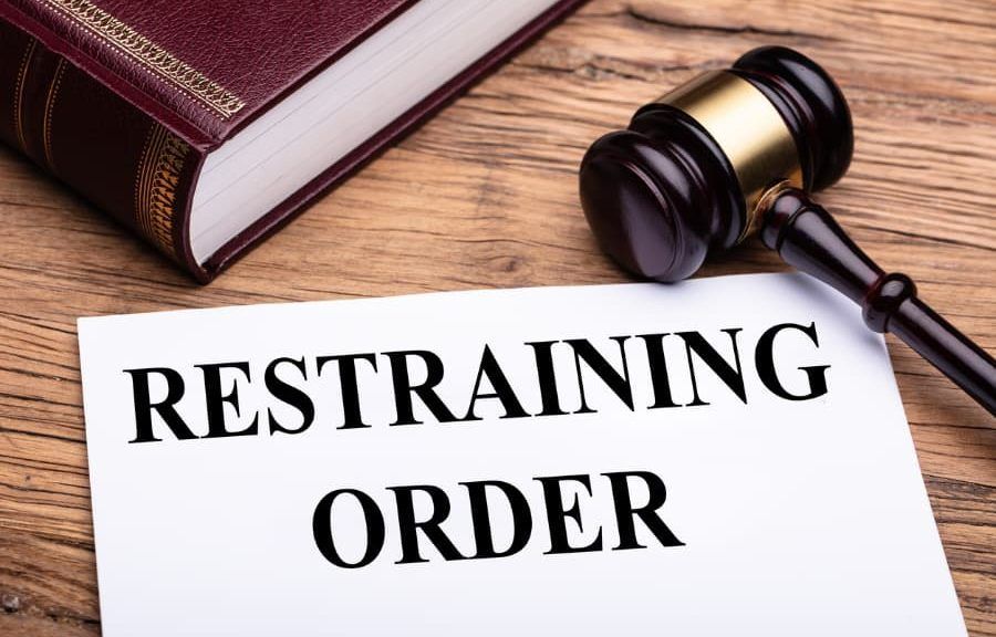 A judge 's gavel is sitting on a wooden table next to a sign that says restraining order.