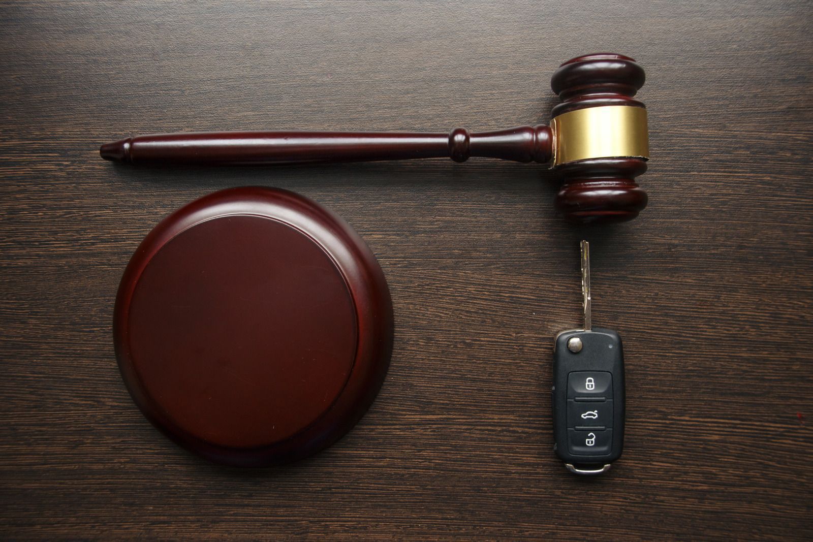 Judge’s gavel, round sounding block, and car key fob on a dark wooden surface.