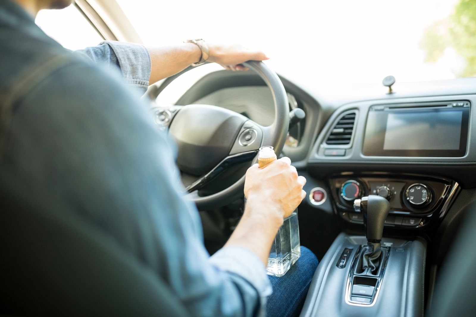 A man is driving a car with a bottle of water in his hand.
