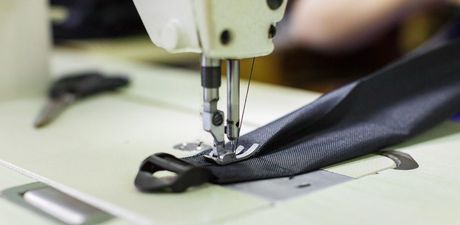 Una macchina da cucire che cuce un cinturino di tessuto nero con una fibbia di plastica.