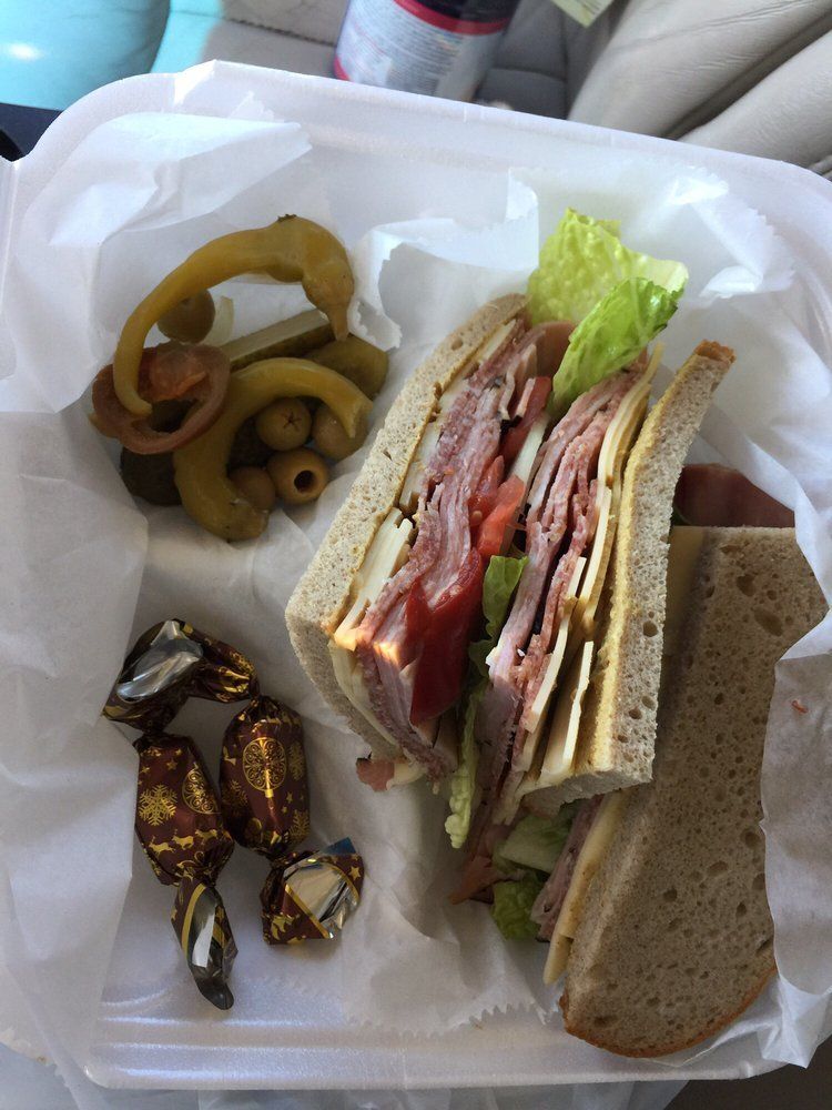Sandwich with lettuce and meat, chips, olives, and wrapped candies in a white takeout container