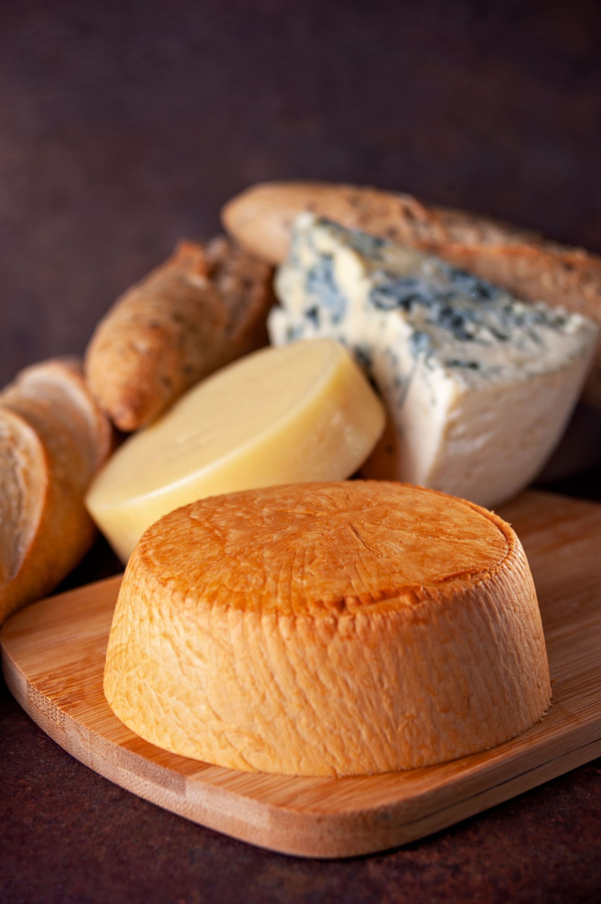 Assorted cheeses on a wooden board, including a blue cheese wedge and a round wheel in the foreground