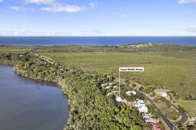 Aerial view of a coastal landscape. A lake is on the left, with houses and a road in the foreground. The ocean is in the background.