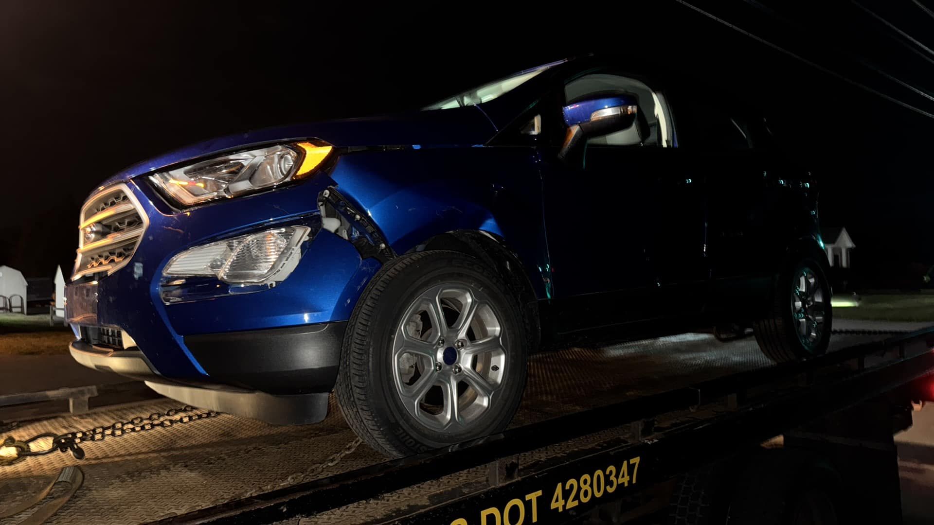 Blue SUV on a tow truck at night, damaged front end.
