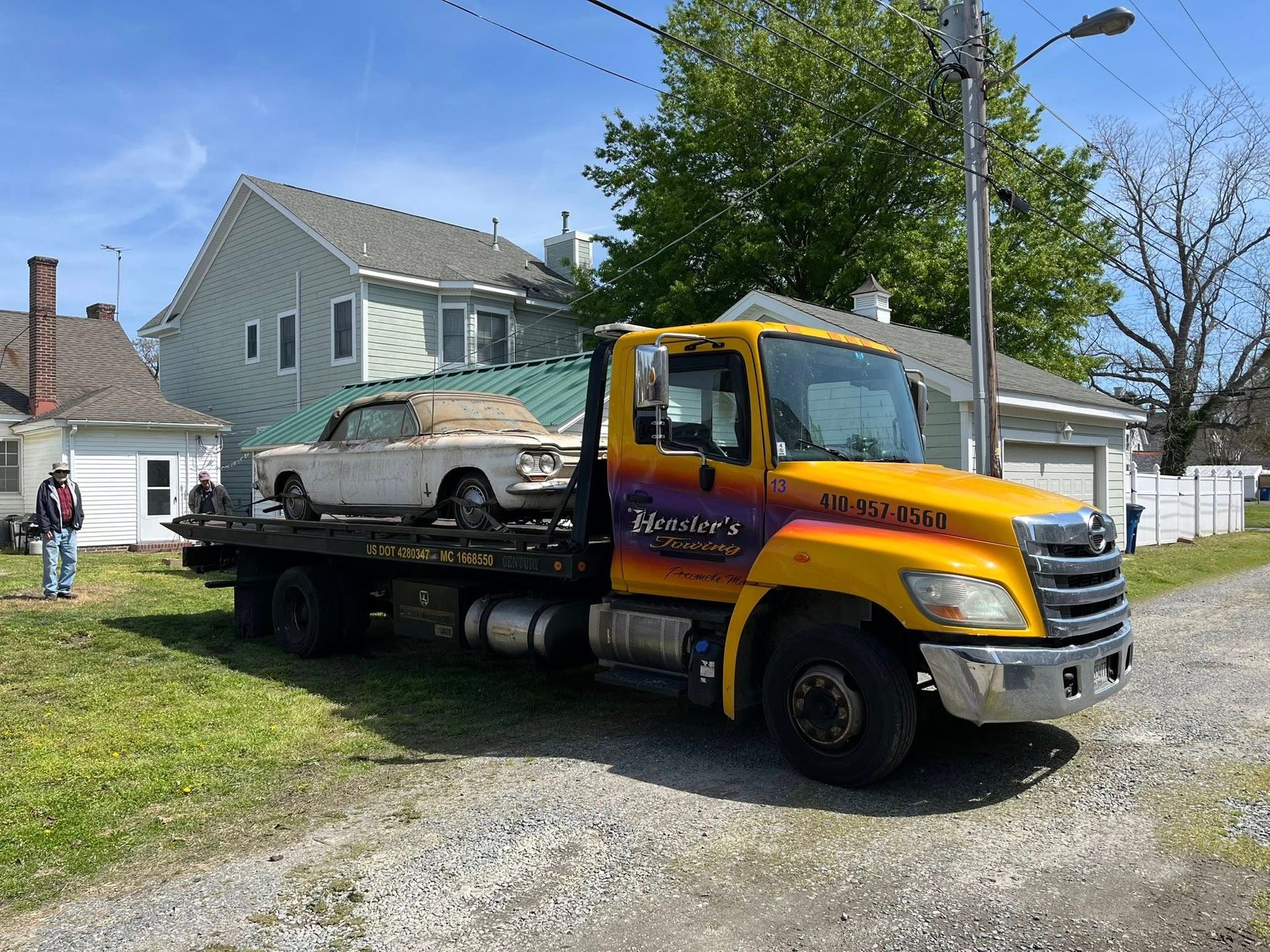Yellow tow truck carrying a white convertible on a residential street.