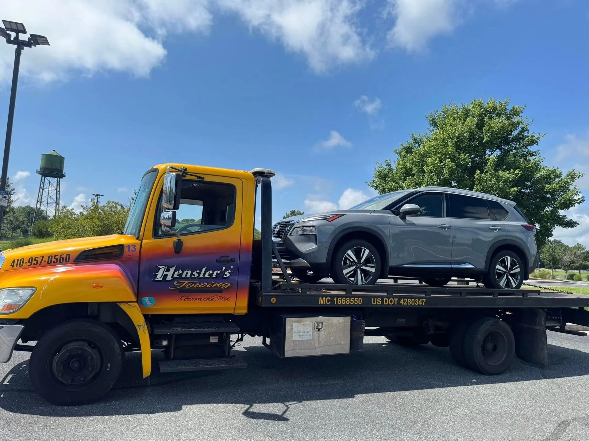Yellow tow truck carrying a gray SUV under a blue sky