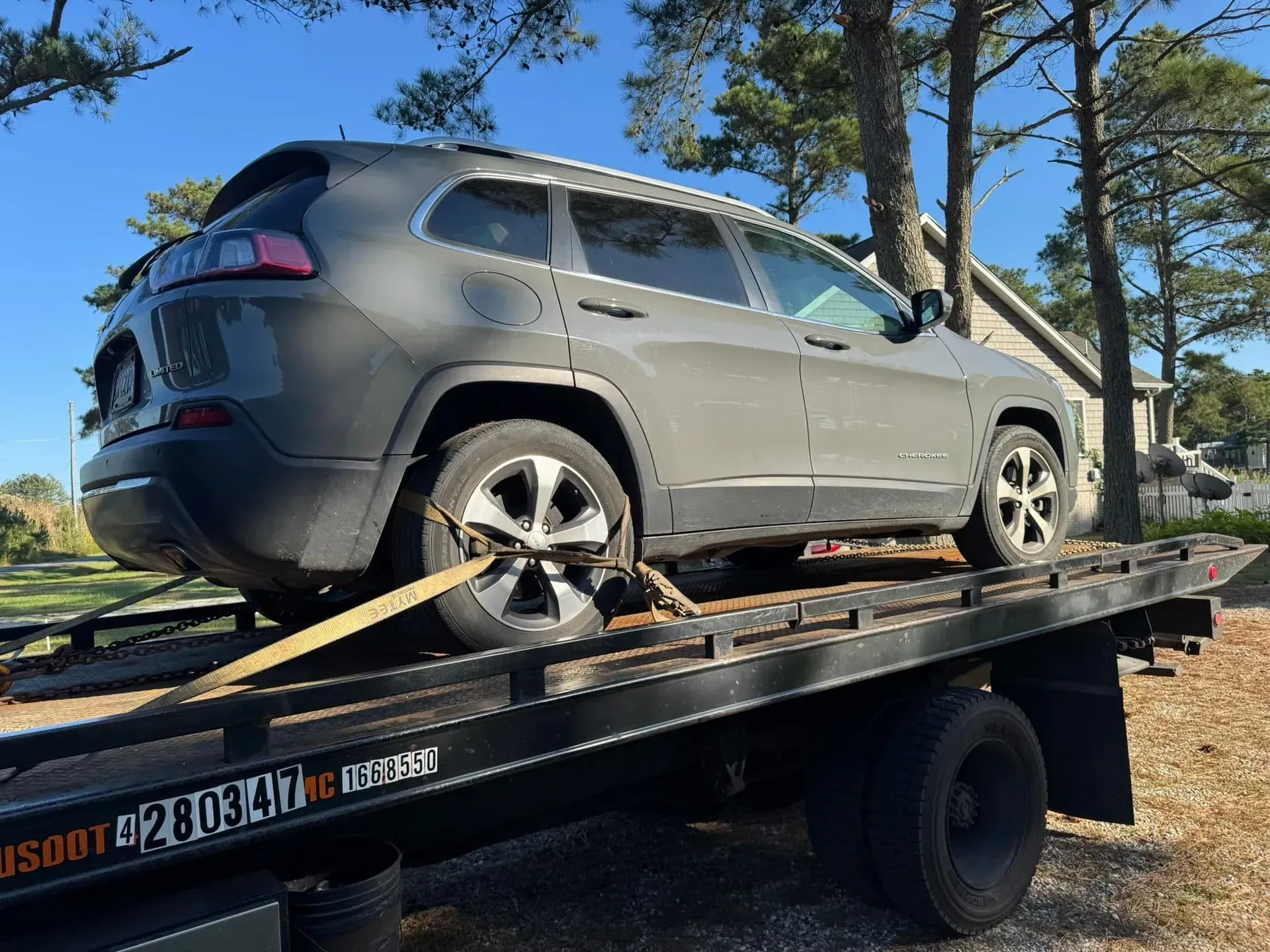 Gray Jeep Cherokee SUV being towed on a flatbed truck on a sunny day.