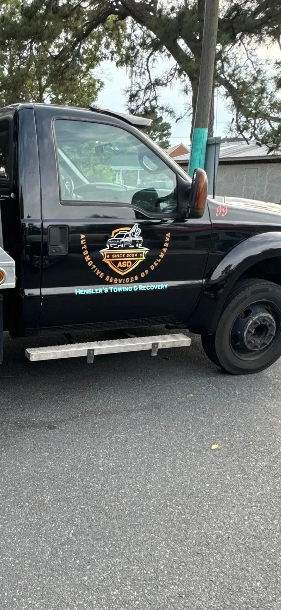 Black tow truck parked on asphalt. The truck has a company logo on the door.