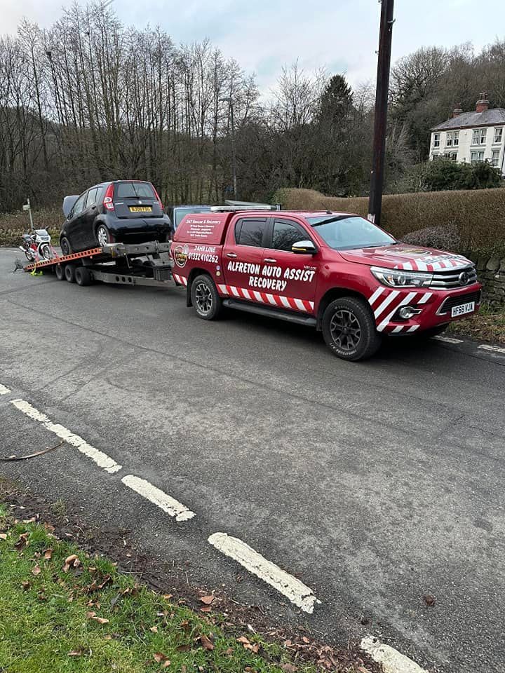 A red truck is towing a car on a trailer down a road.