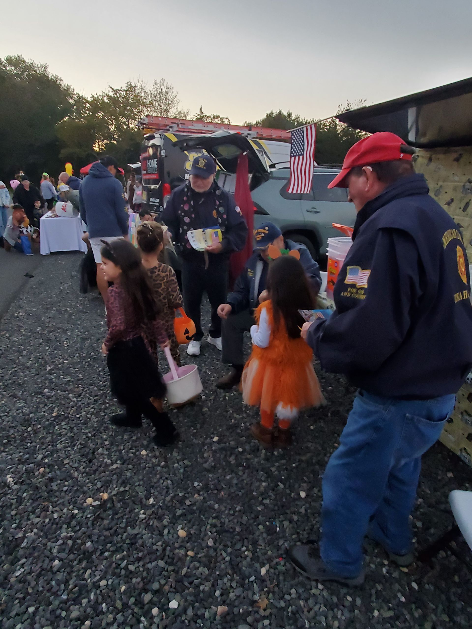 Children in costumes receive candy at a trunk-or-treat event with adults and decorated vehicles.