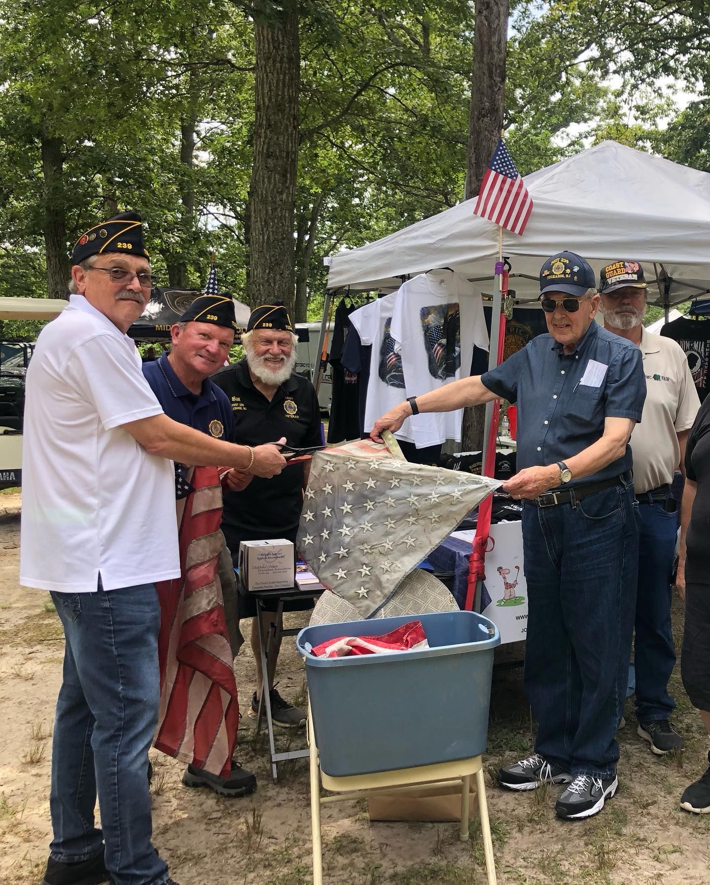 Veterans folding a U.S. flag at an outdoor event with a merchandise tent.