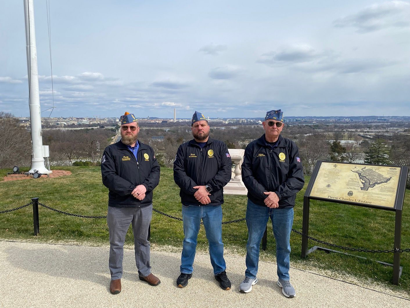 Three people in uniform stand on a hill with a city view in the background.
