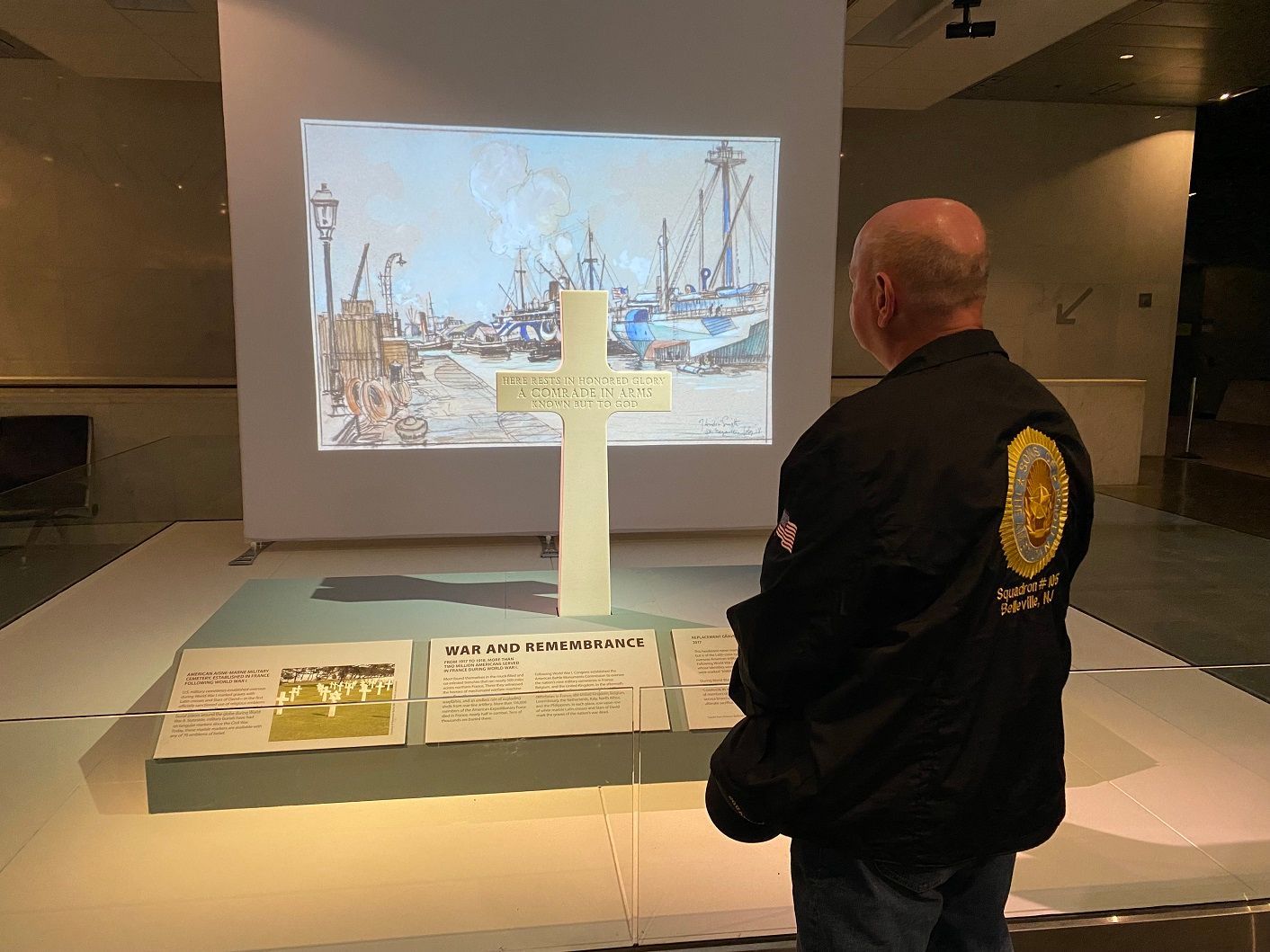 Man viewing a museum exhibit. A large cross stands before a projected painting and informational plaques.