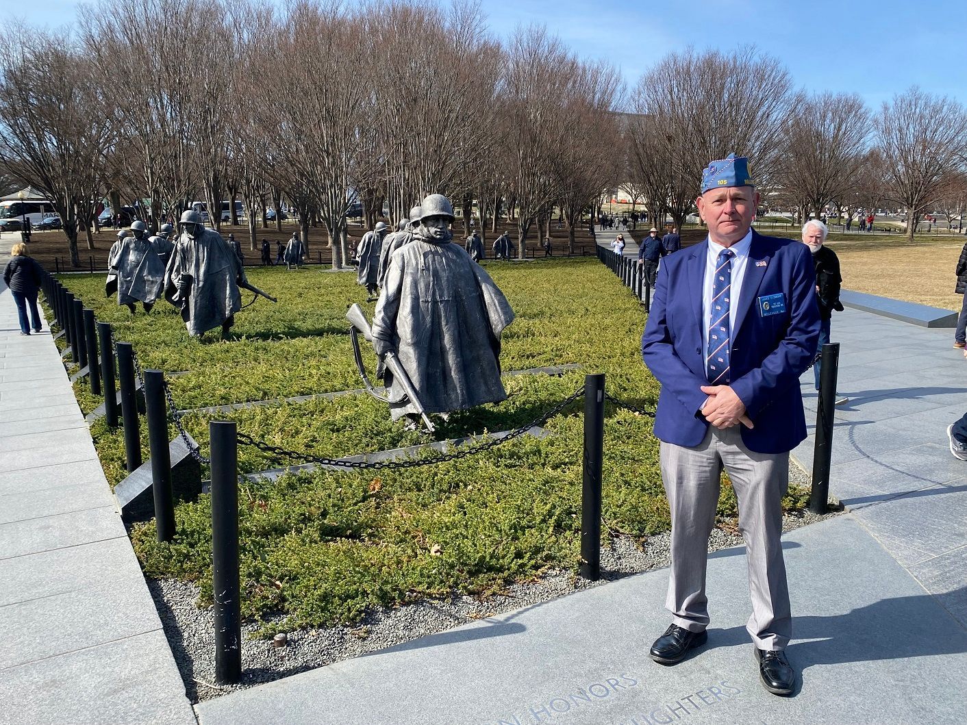 Man in blue blazer stands at the Korean War Veterans Memorial, statues of soldiers in the background.