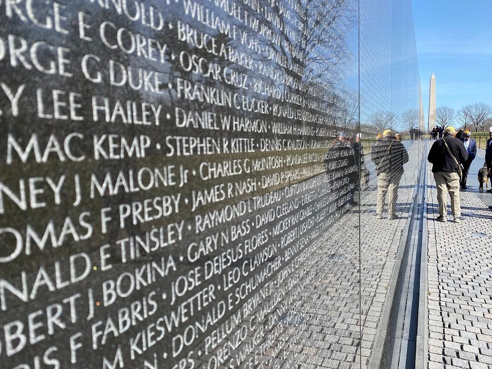 Vietnam Veterans Memorial wall with names etched in granite; people walk nearby.