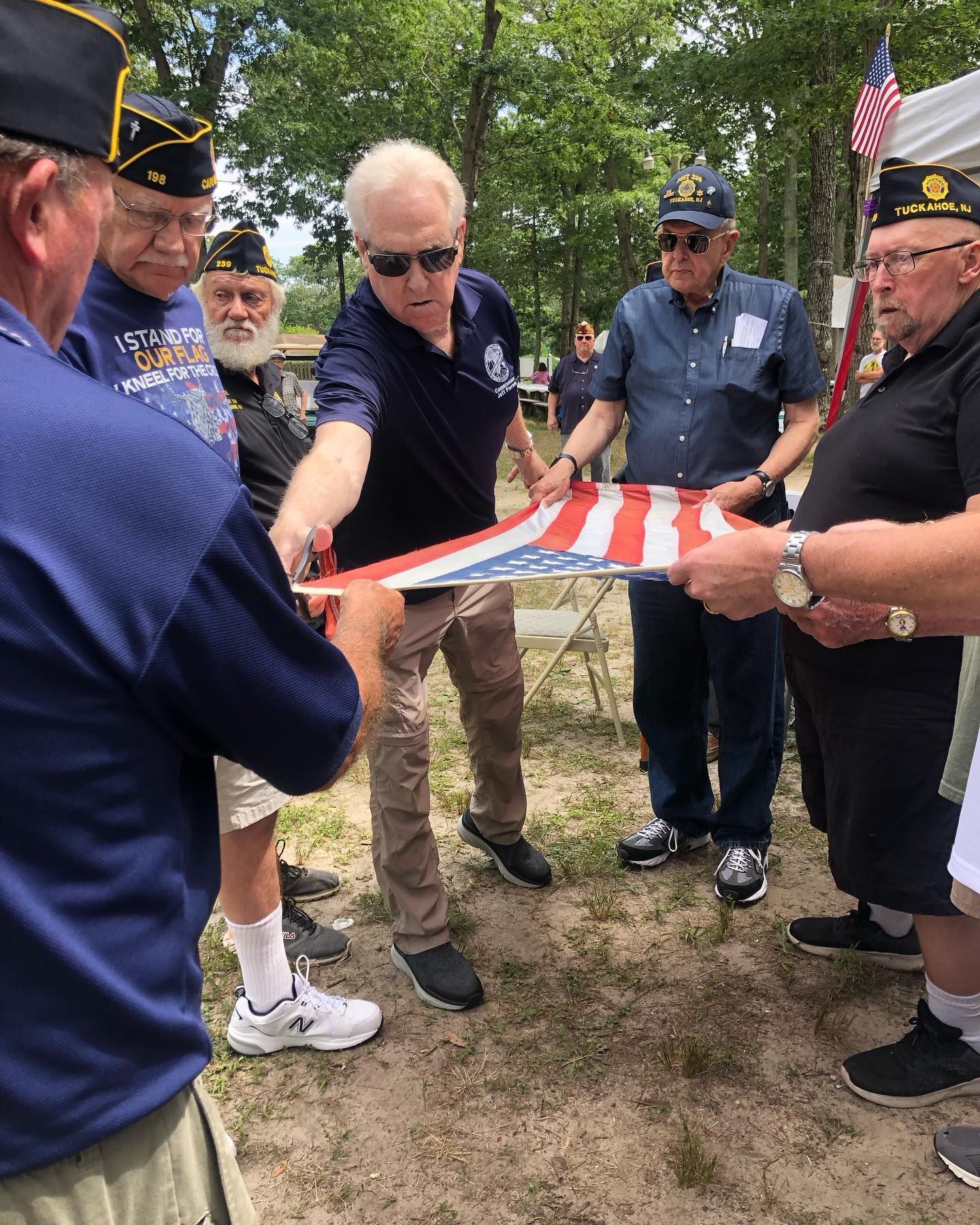 Veterans folding an American flag outdoors. Men wearing hats, holding flag during ceremony.