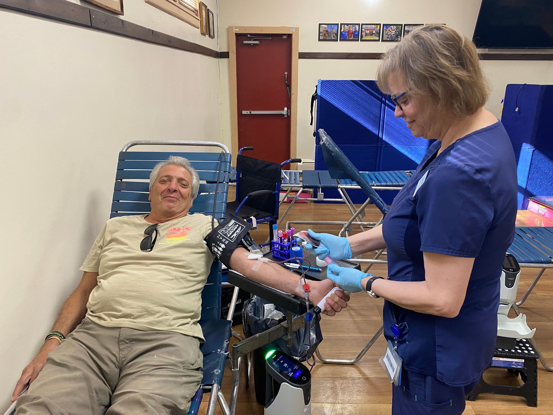 A woman in scrubs draws blood from a man in a chair at a donation center.