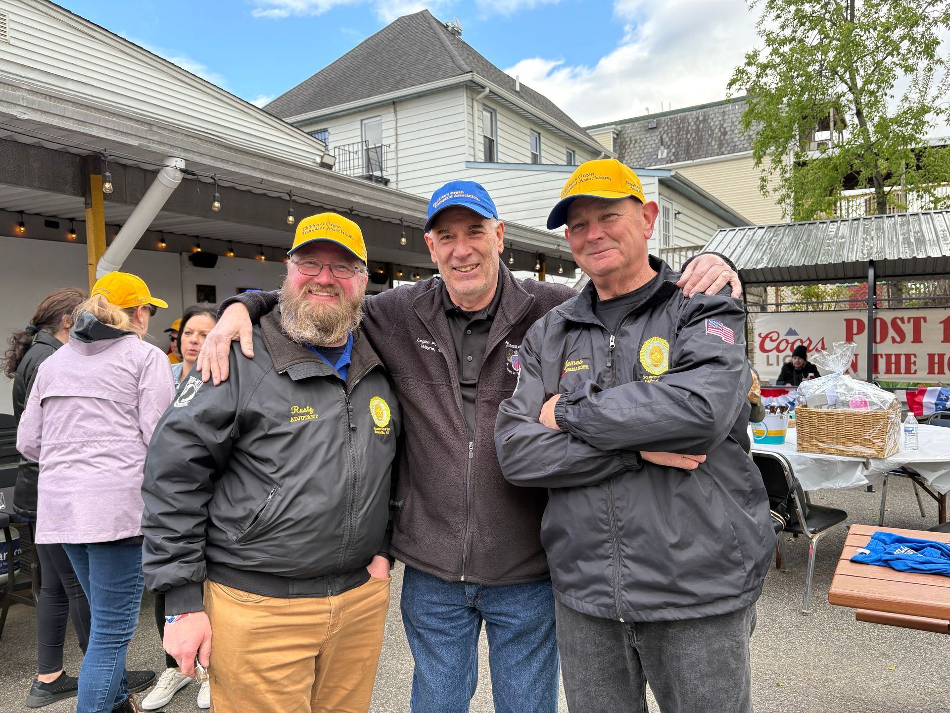 Three men in jackets and hats pose outside, arms around each other.