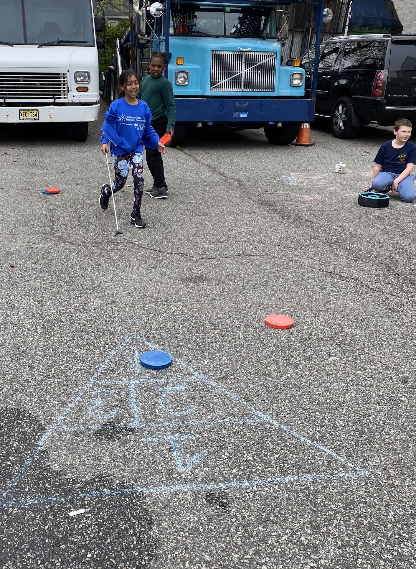Children playing a game with frisbees on a concrete surface. A girl with crutches is running; other children are nearby.