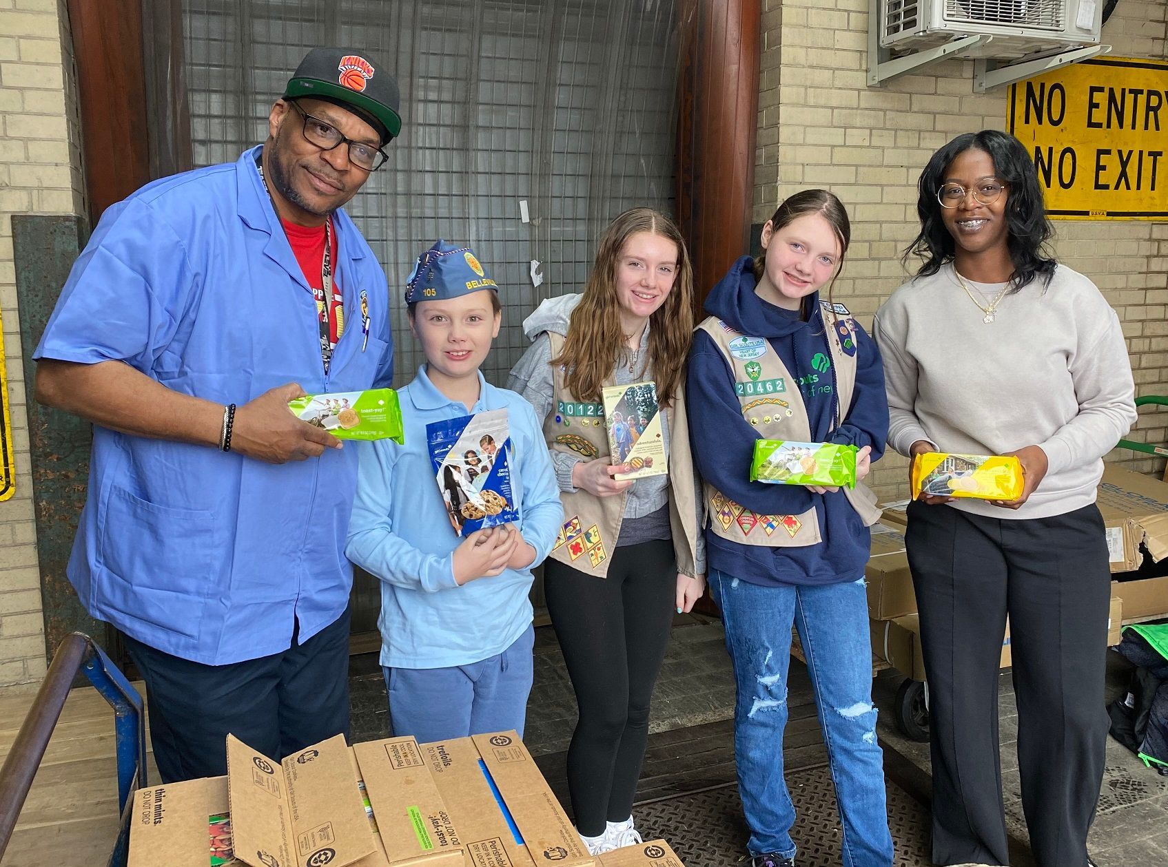 Group of people posing with boxes and snacks in front of a building.