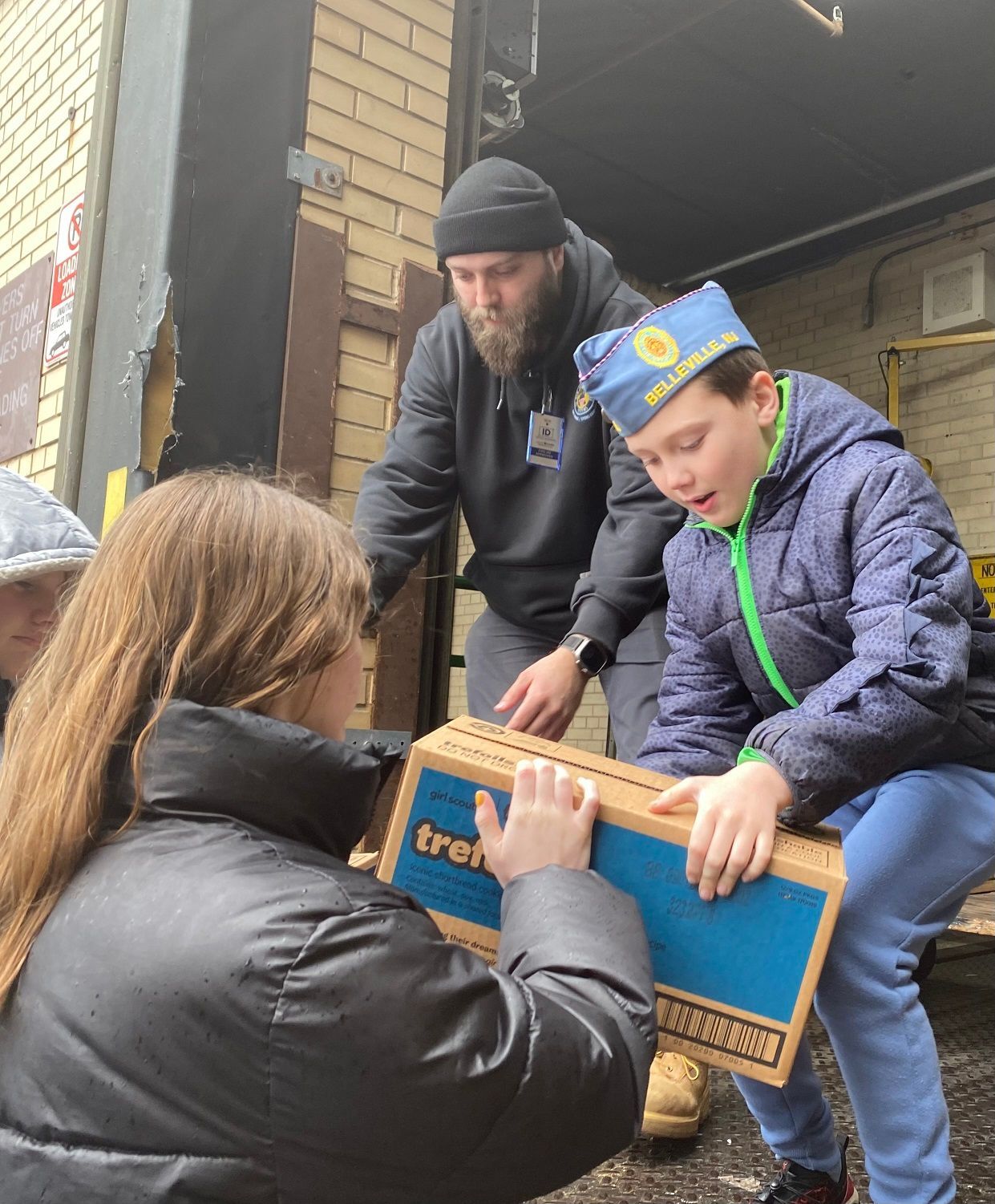 People loading a box. The setting is outside a building with a loading dock.