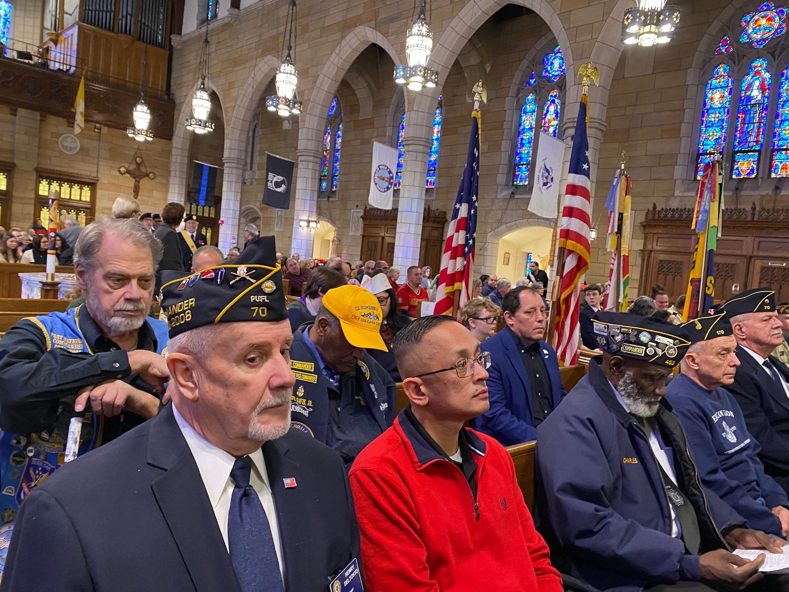 Veterans in a church, flags on display, people seated, some wearing service caps.