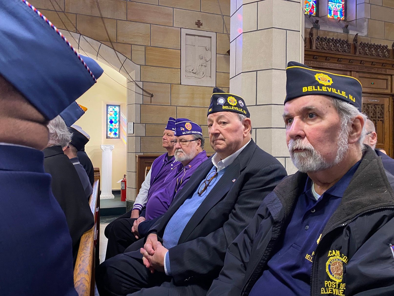 Veterans in uniform caps sit in church pews during a ceremony.
