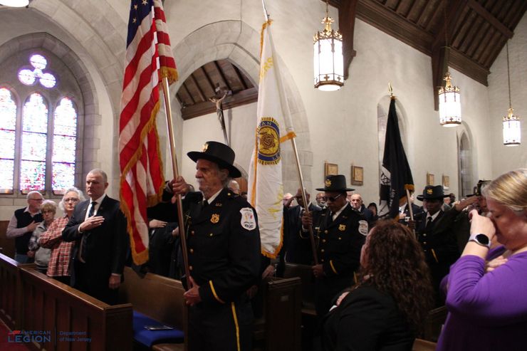 Inside church: Honor guard carrying flags; people standing and watching.