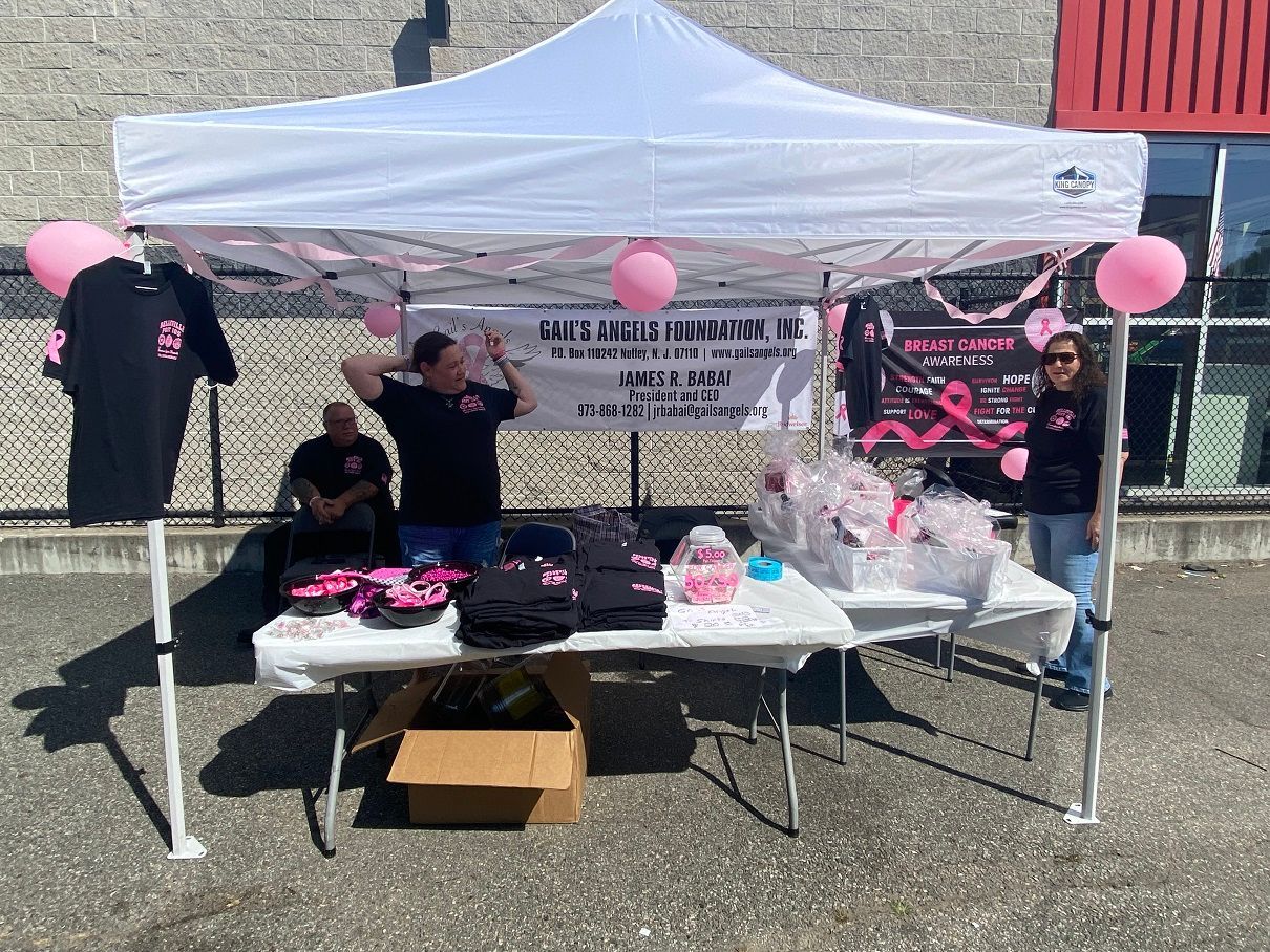 A breast cancer awareness booth with volunteers under a white tent; pink decor, merchandise.