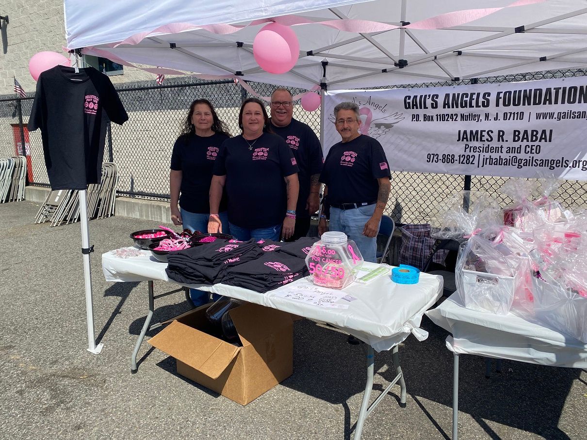 People at a breast cancer awareness booth with pink and black merchandise, a banner, and pink balloons.
