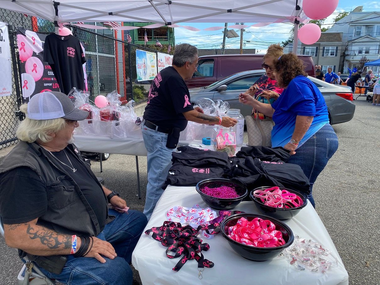 People at a table selling pink ribbon items for breast cancer awareness at an outdoor event.