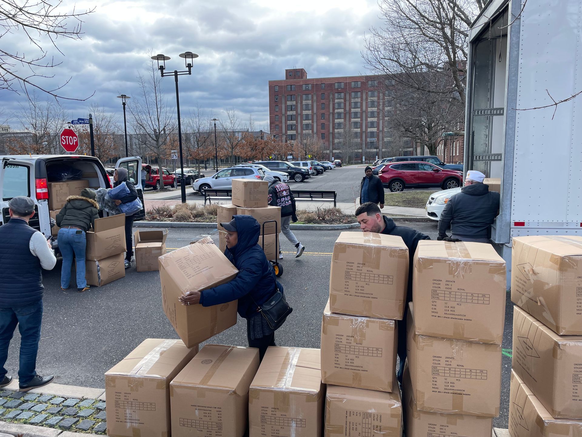 People unloading boxes from a truck and van in a parking lot.