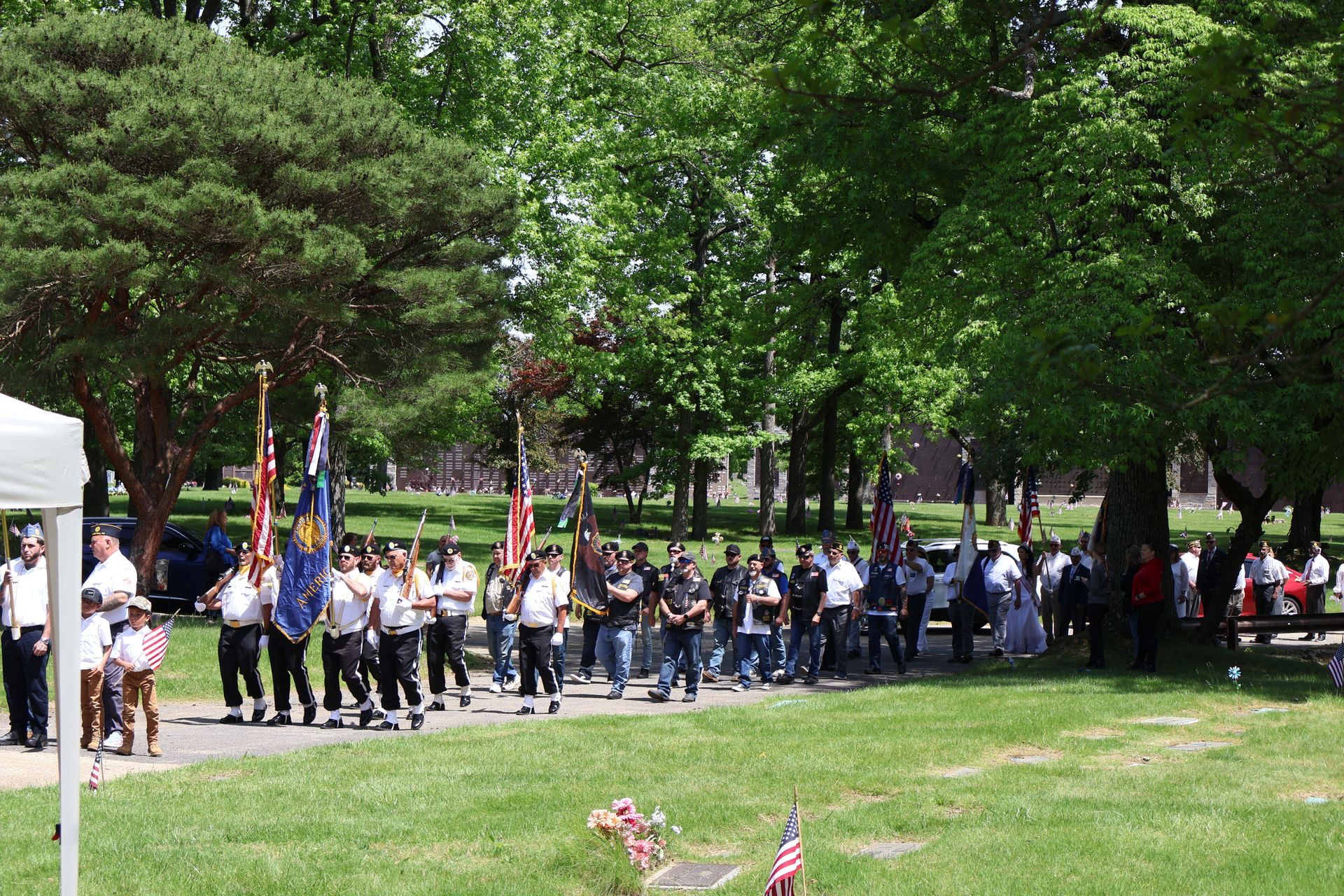 People marching with flags along a park path, with trees and spectators nearby