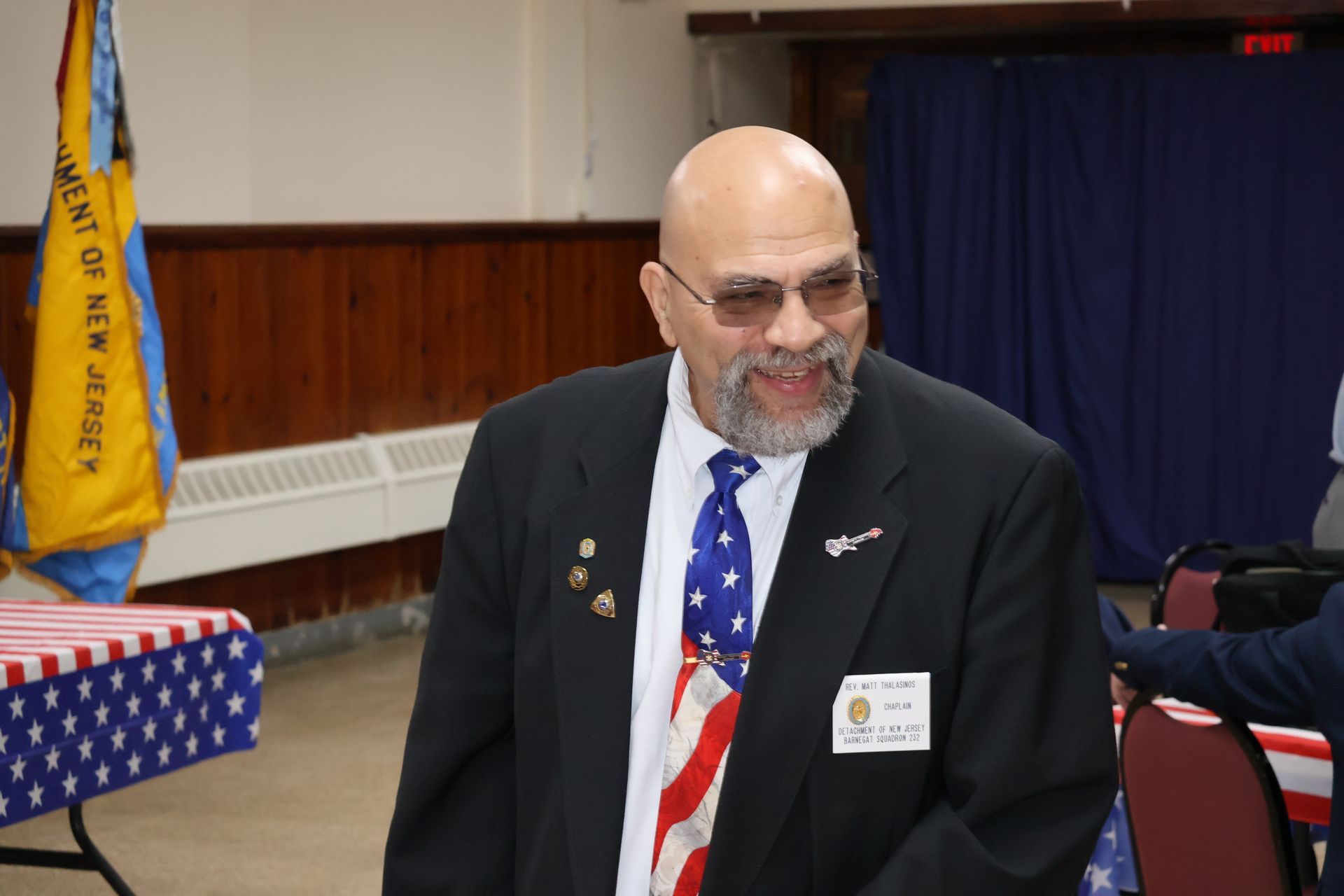 Man in suit with American flag tie; indoor event.