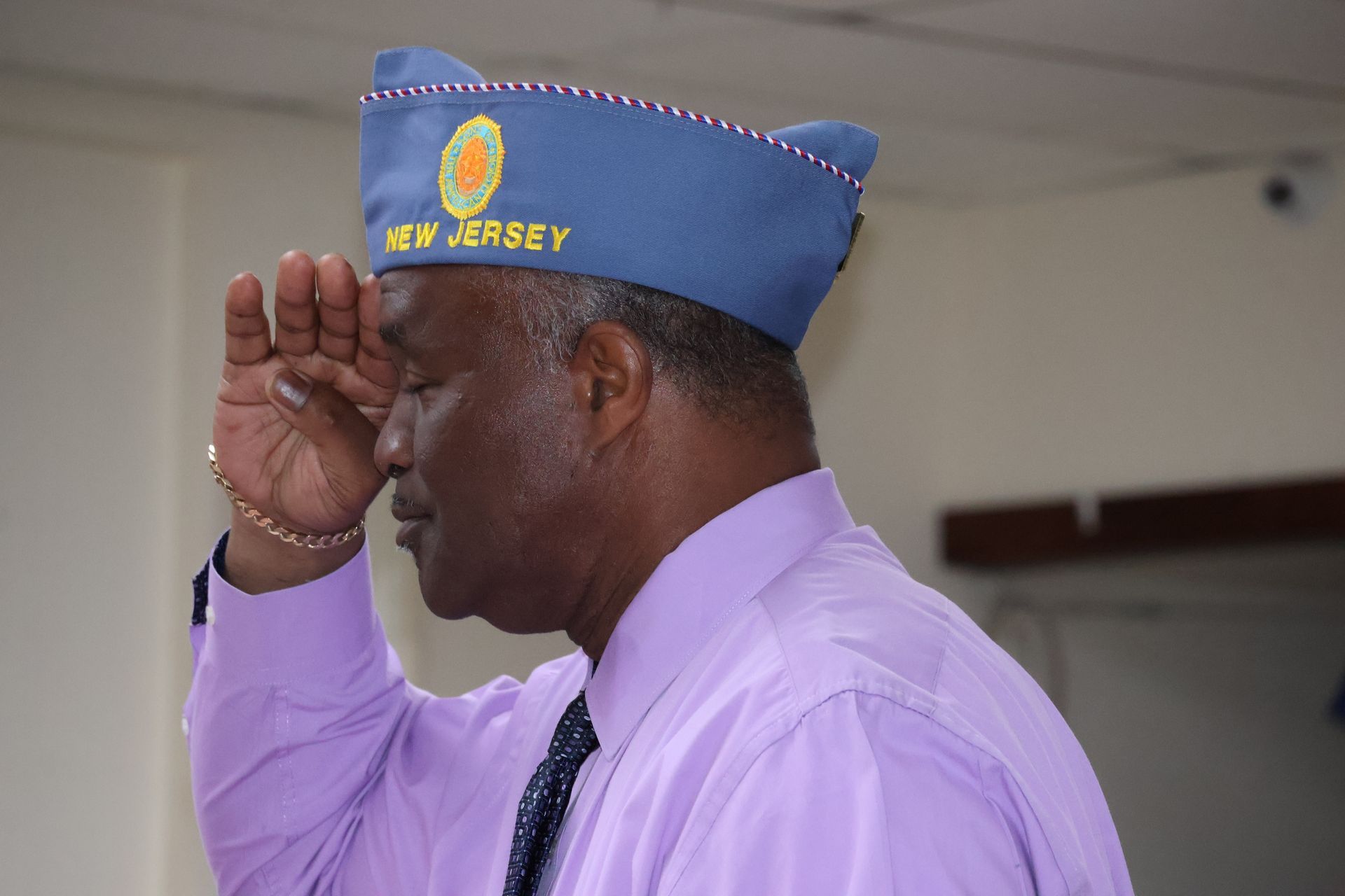 Man in blue cap saluting. Cap reads 