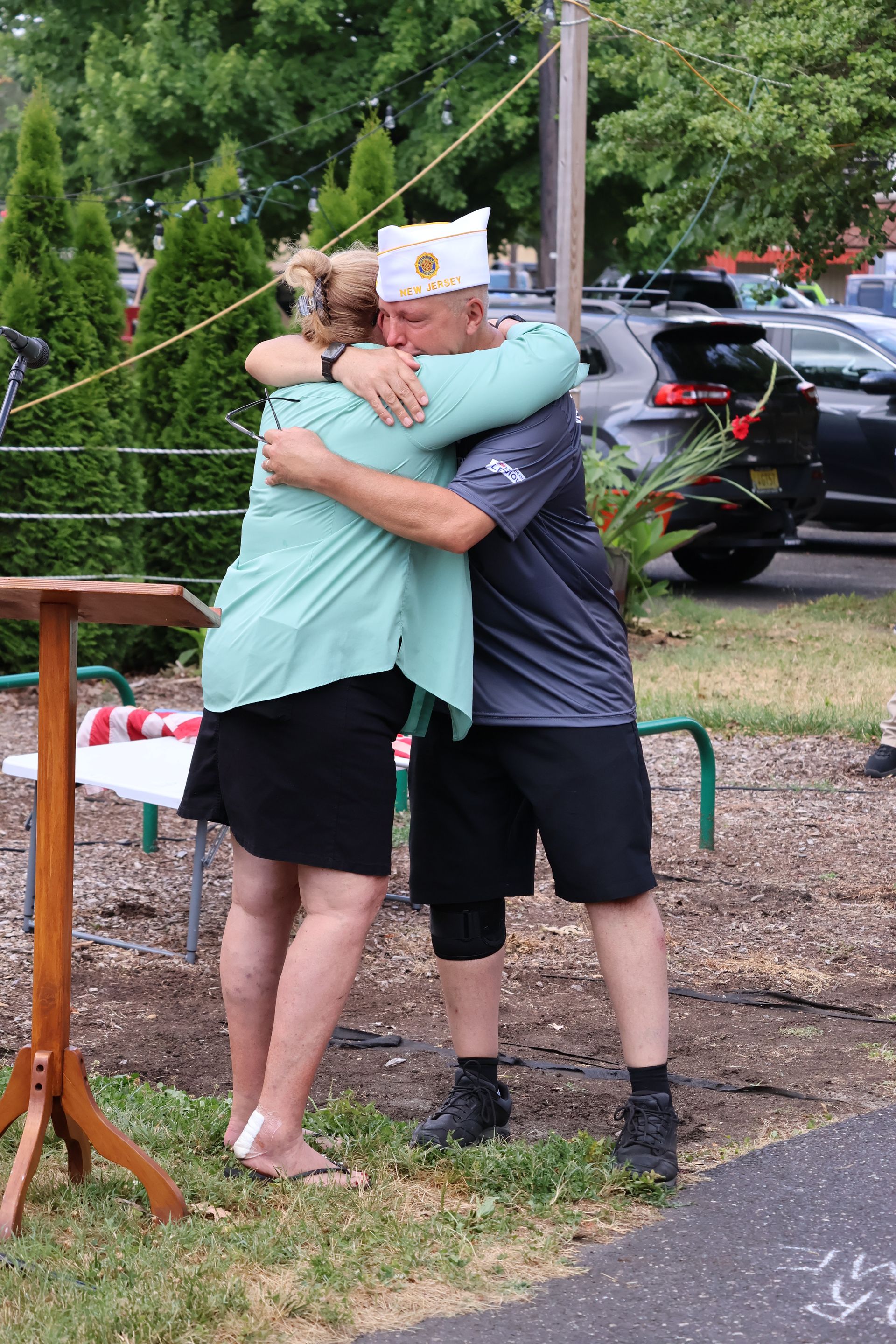 A woman and a man in a military hat embrace outdoors.