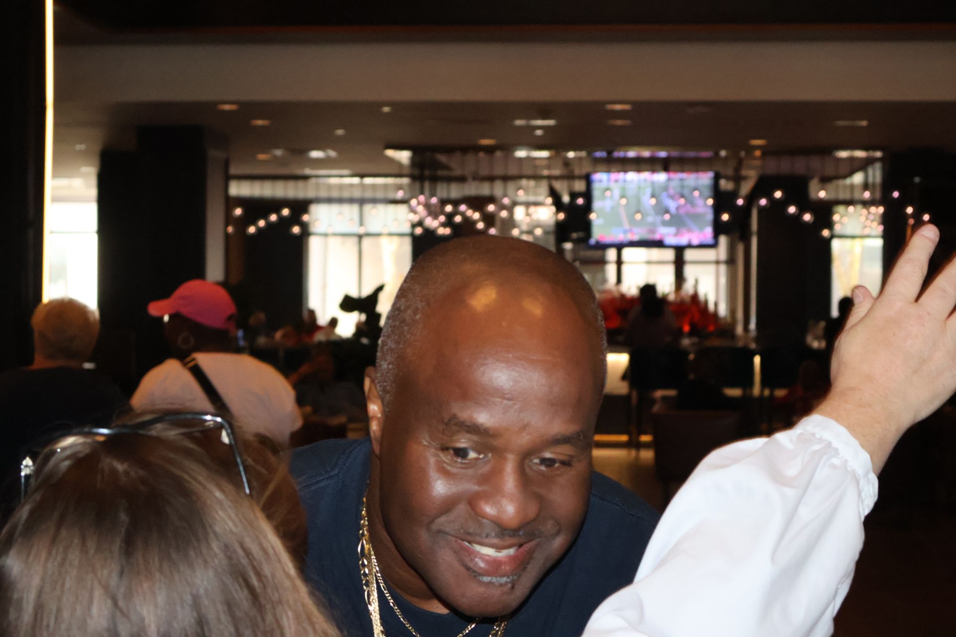 Smiling man in a dark top, inside a brightly lit public space, looking down.