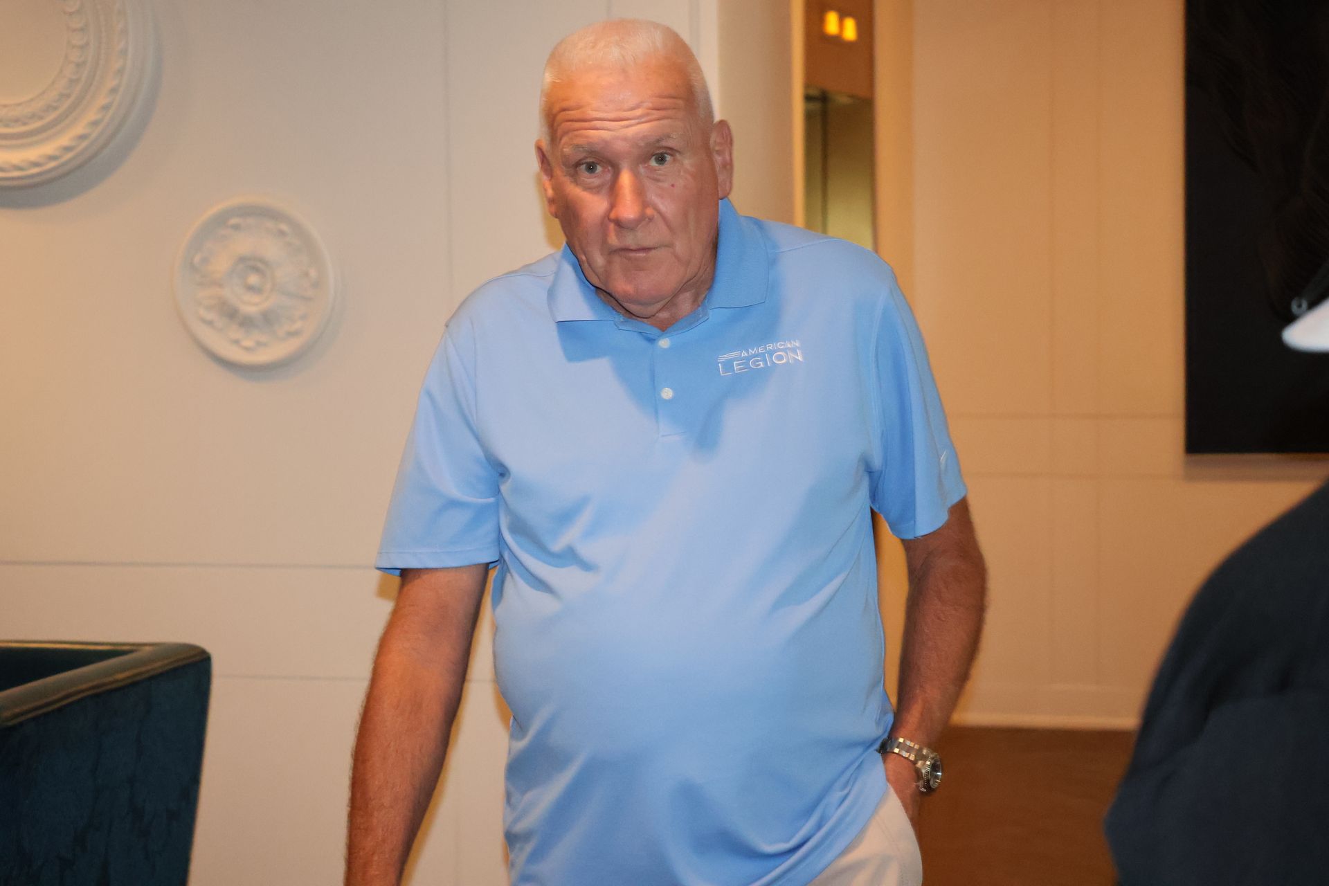 Man in light blue polo shirt stands indoors, looking forward.