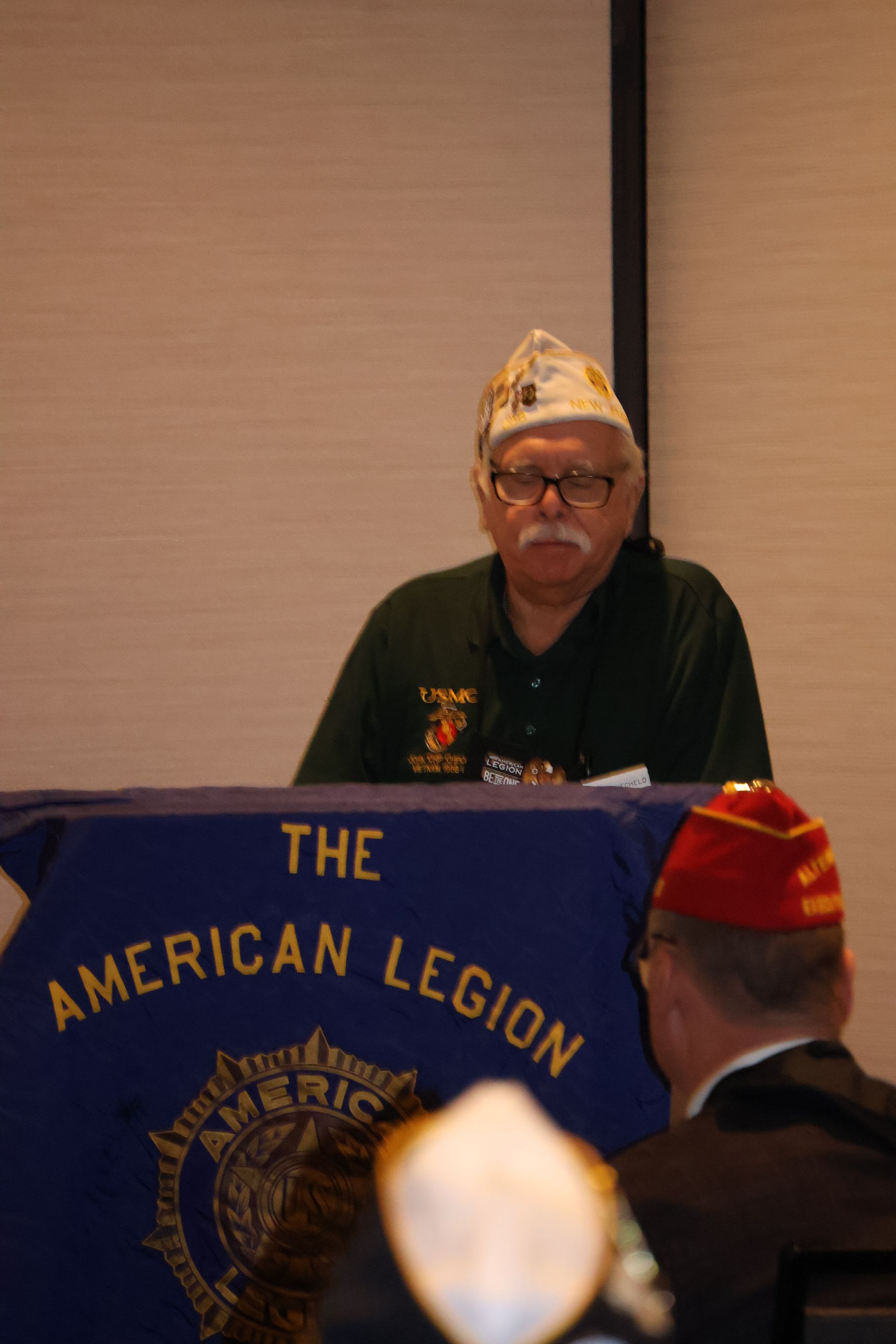 Man in green shirt and hat, at a table with 