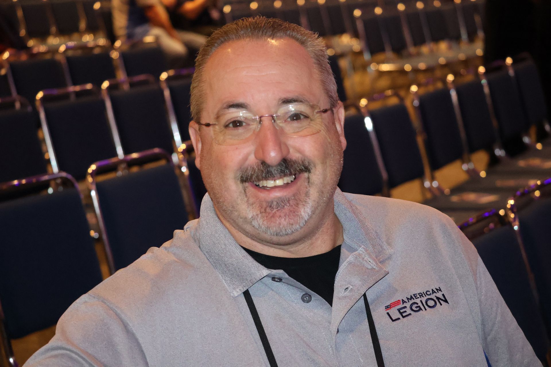 Man with glasses smiling, wearing a gray shirt with 