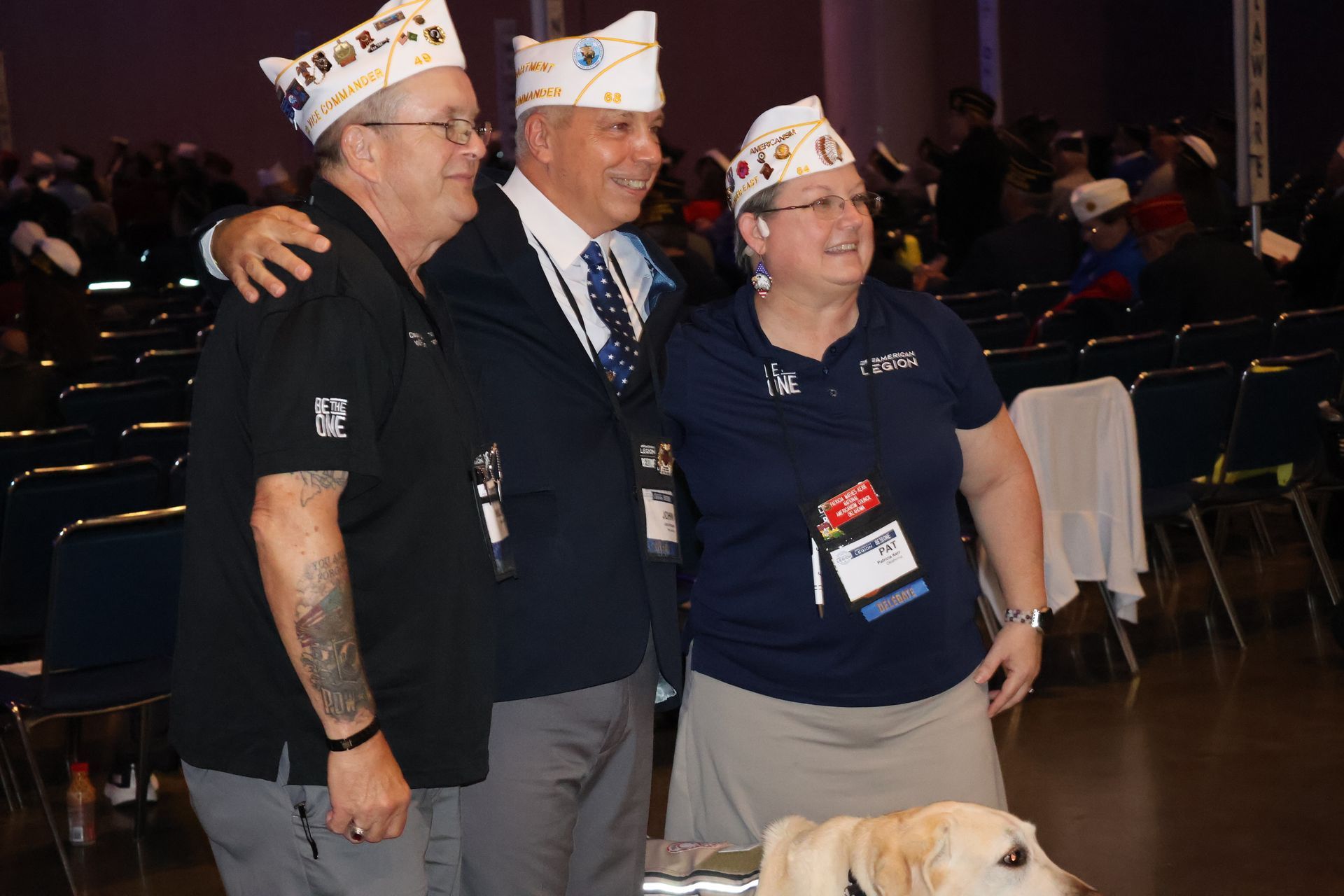 Three people in white caps pose, smiling, with a dog, at an event.
