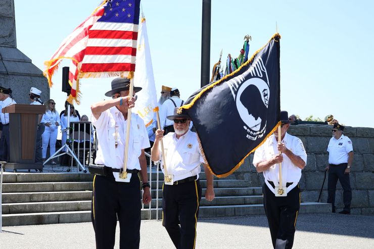 Veterans holding flags, including American flag, during outdoor ceremony.