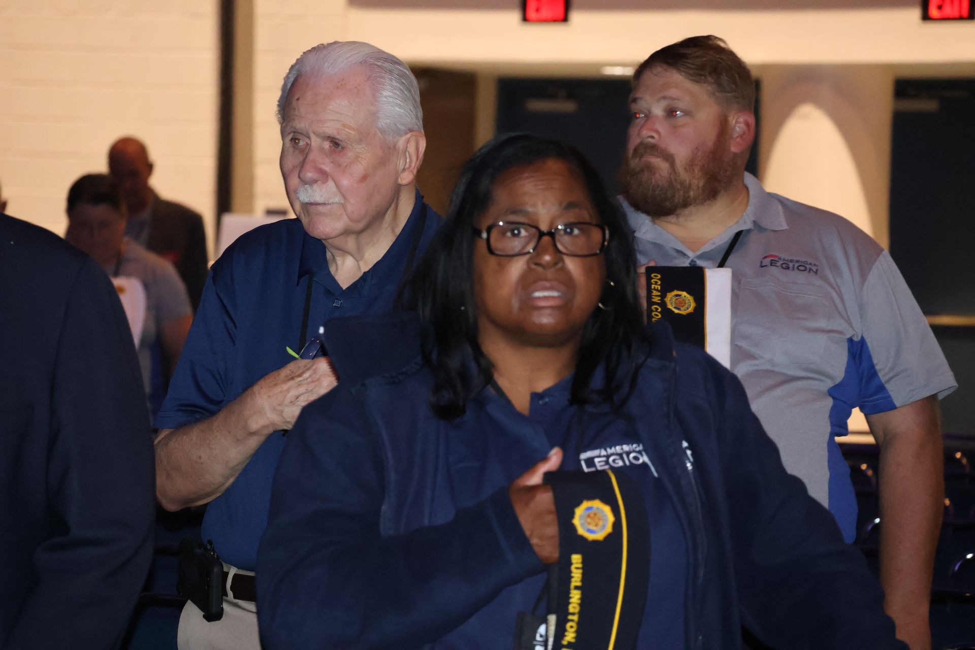 People in a crowded area; woman in blue vest looking forward, older man to her left.