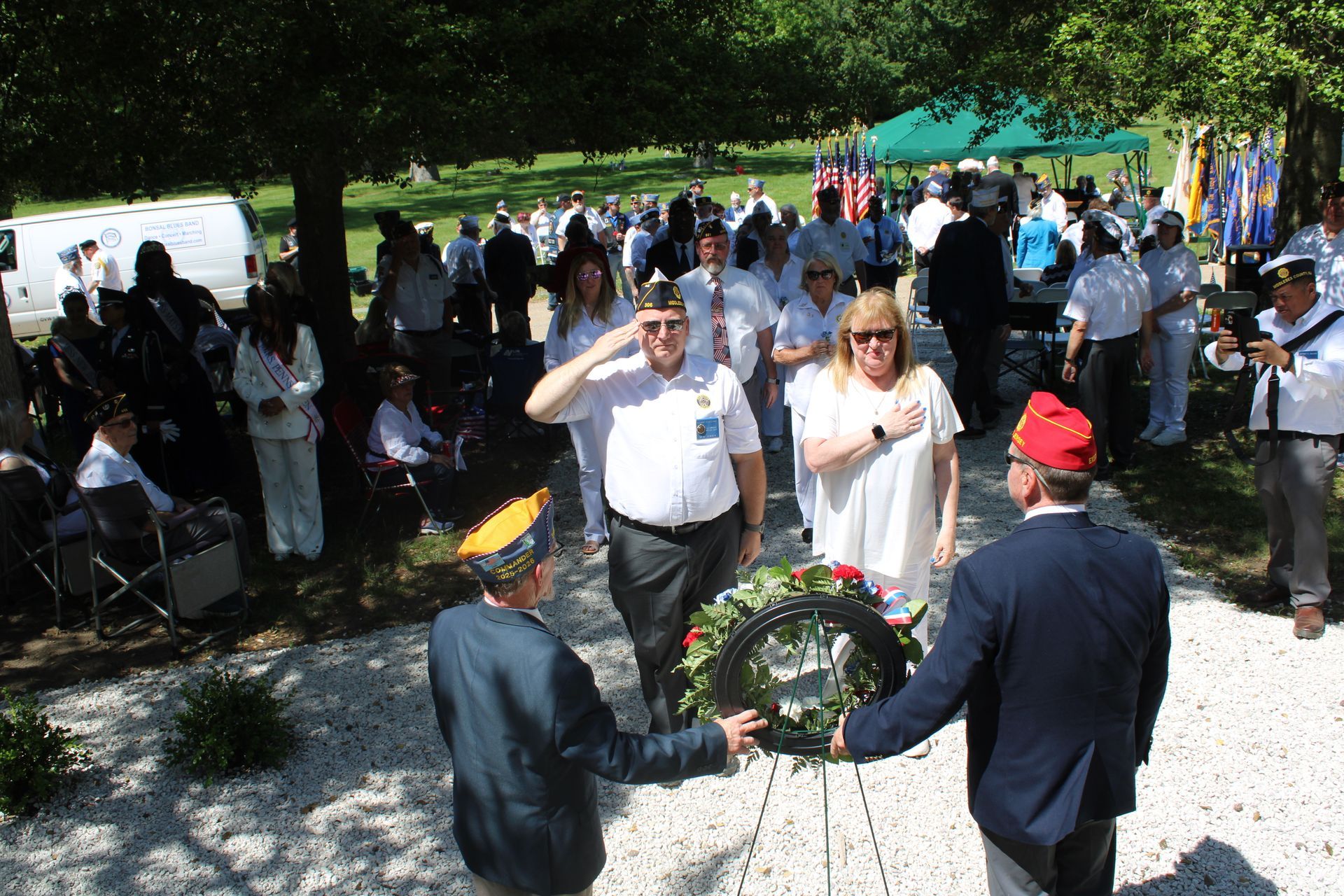 People placing a wreath at a memorial in a sunny outdoor gathering