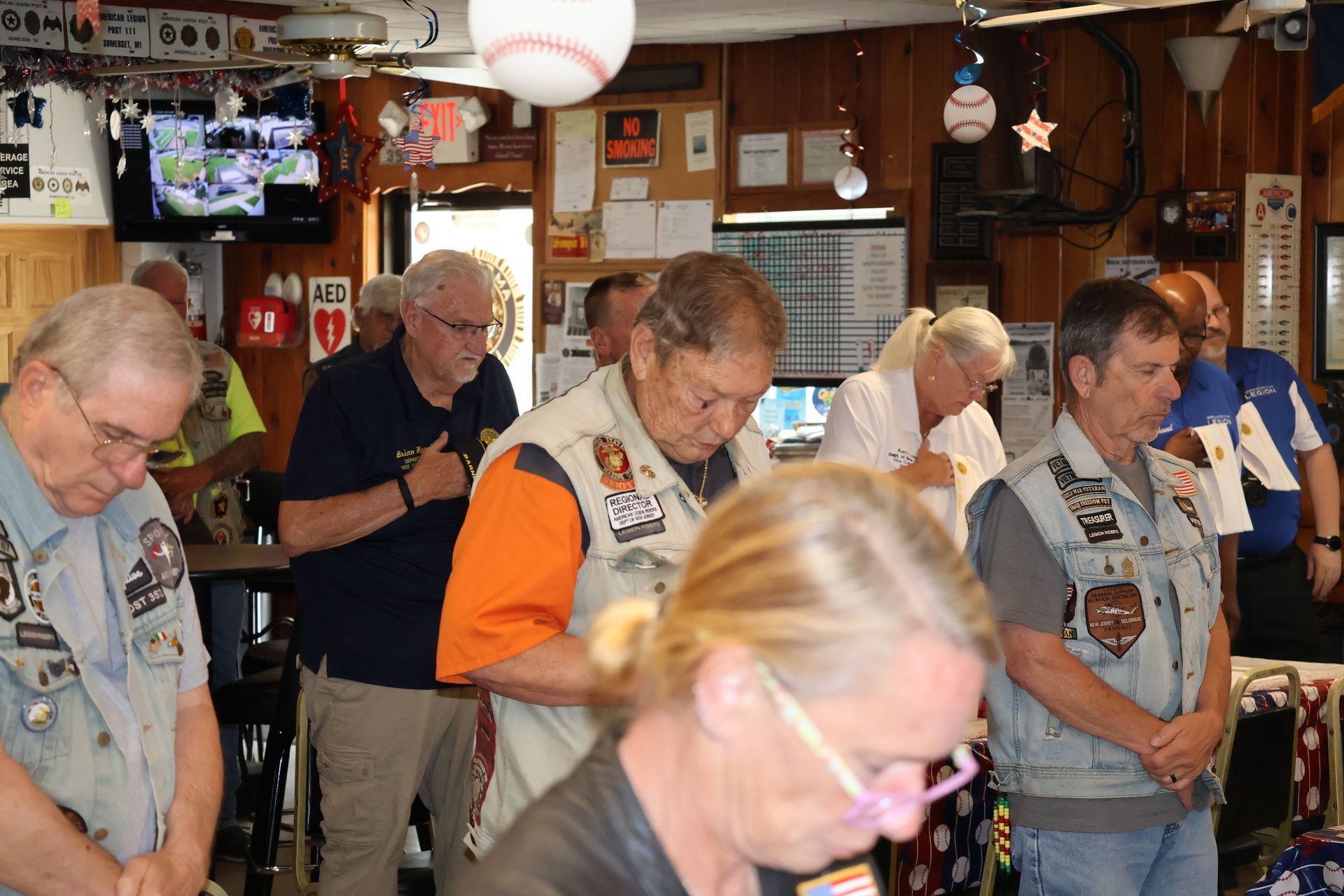 People with heads bowed in a room, some wearing vests, possibly in prayer or reflection.