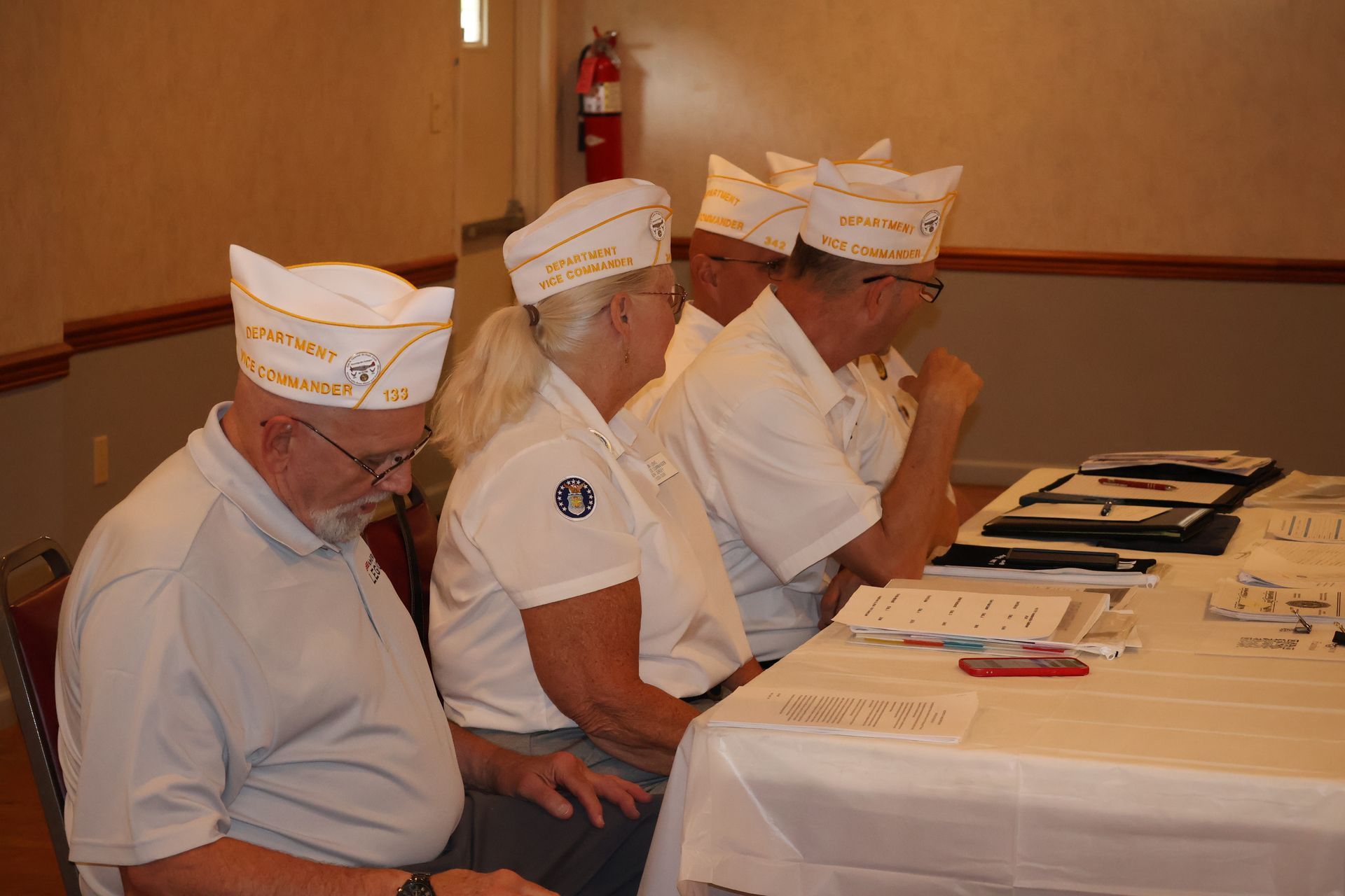 Four people wearing white hats and shirts sit at a table, looking at paperwork.