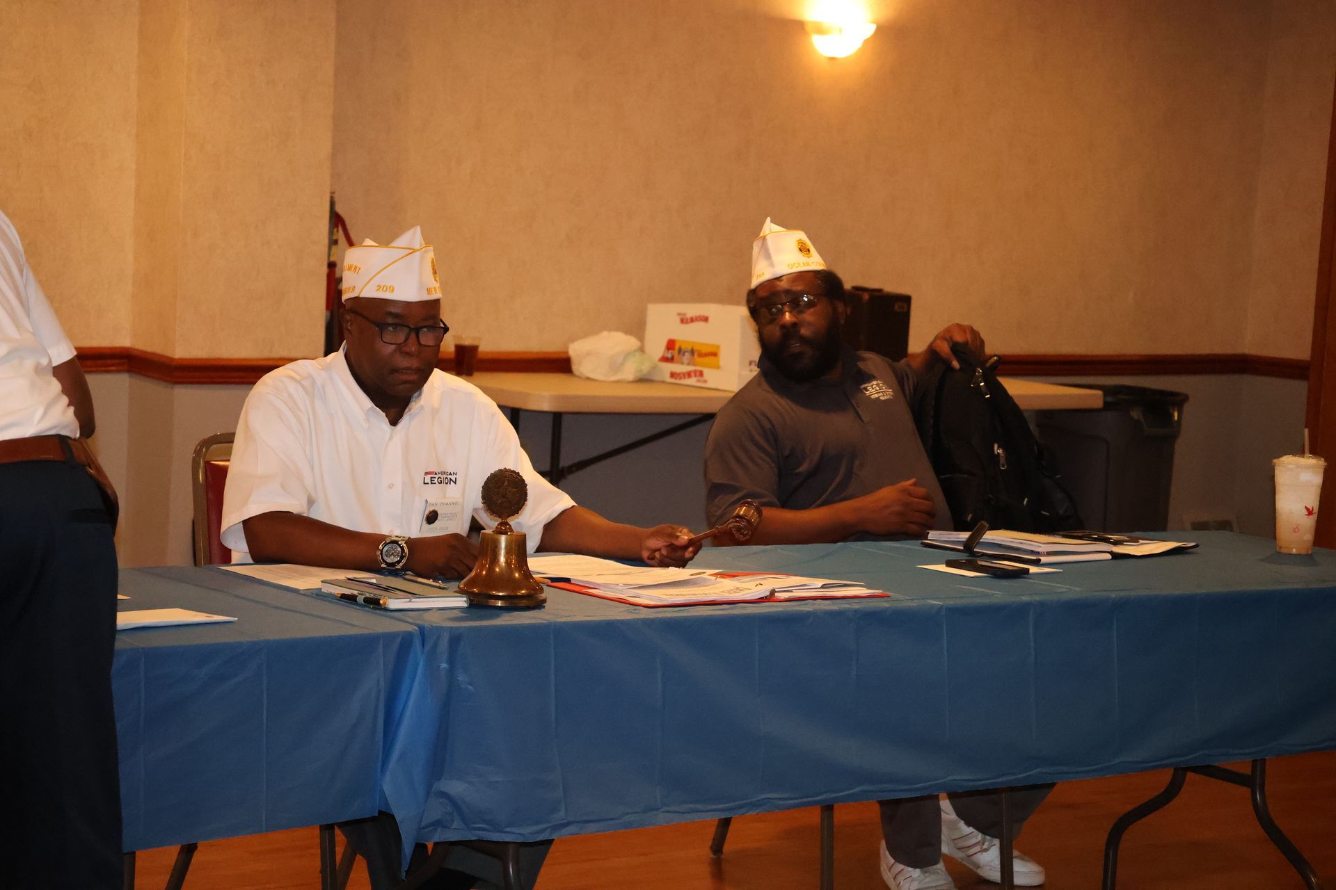 Two men wearing white hats at a blue-covered table, likely at an event.
